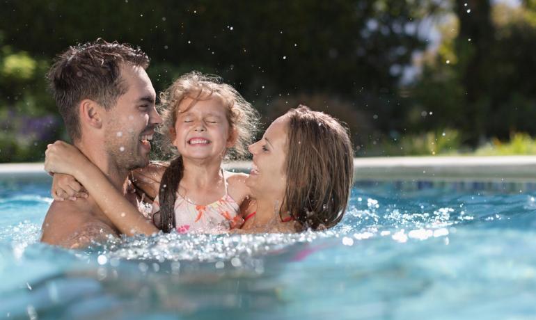 Glückliche Familie spielt im Pool unter der Sonne.