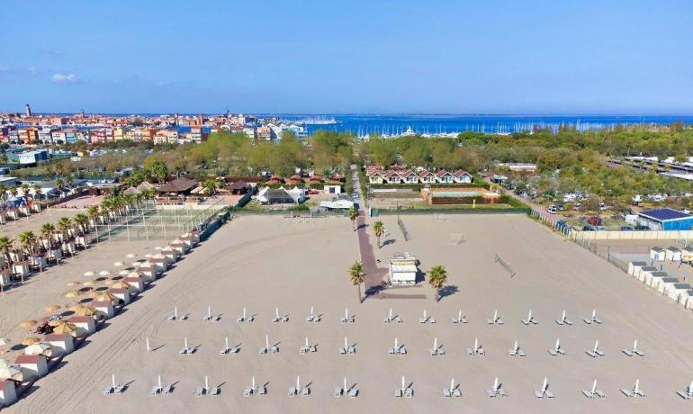 Leerer Strand, geschlossene Sonnenschirme, blaues Meer, ferne Stadt.