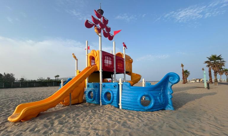 Bunter Spielplatz in Schiffsform an einem sonnigen, ruhigen Strand.