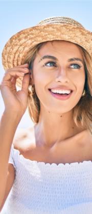 Donna sorridente con cappello di paglia, sfondo marino, giornata soleggiata.