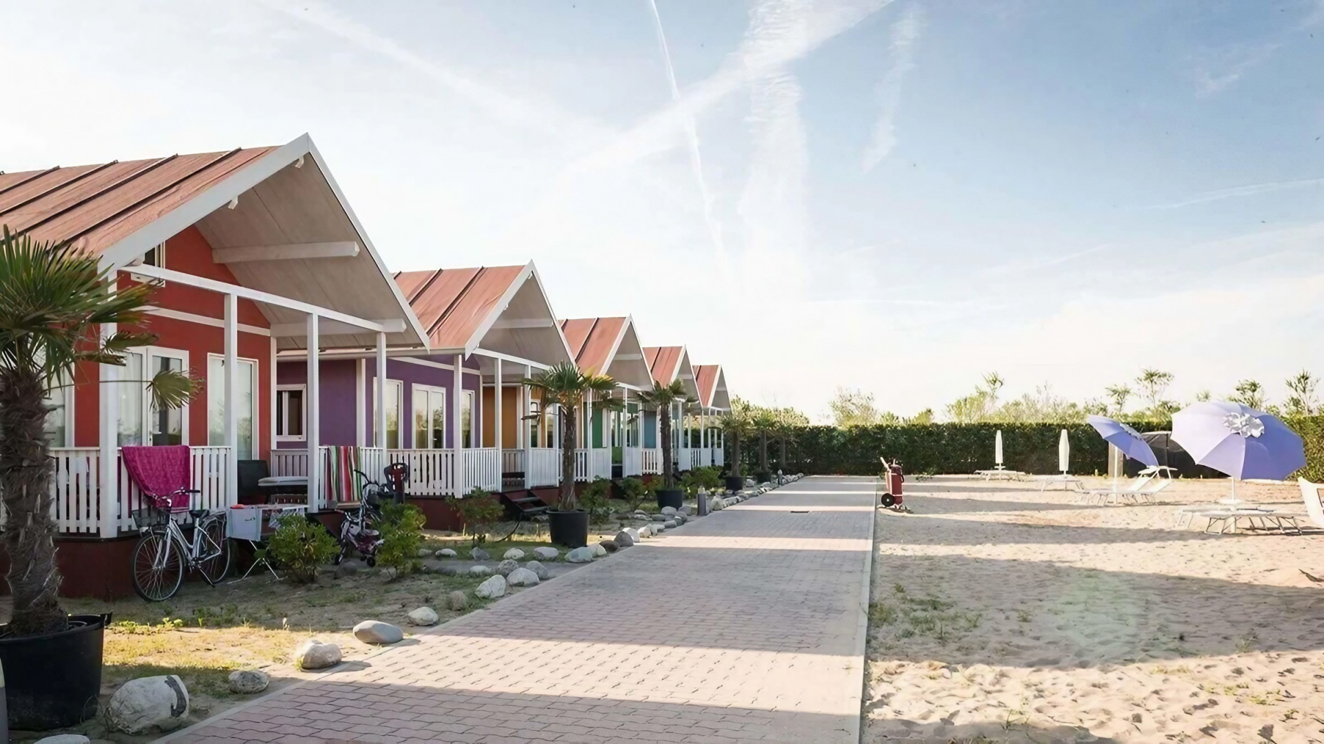 Bunte Strandhütten, blaue Sonnenschirme, entspannte Urlaubsatmosphäre.