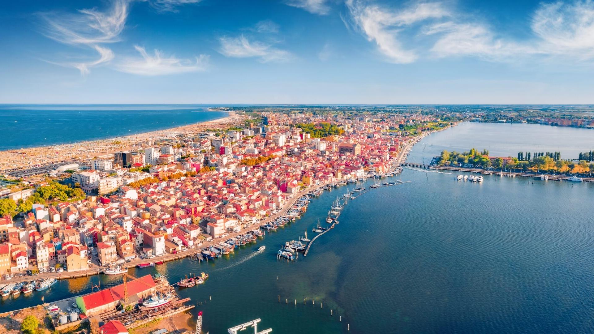 Veduta aerea di una città costiera con spiaggia e porto, cielo sereno.