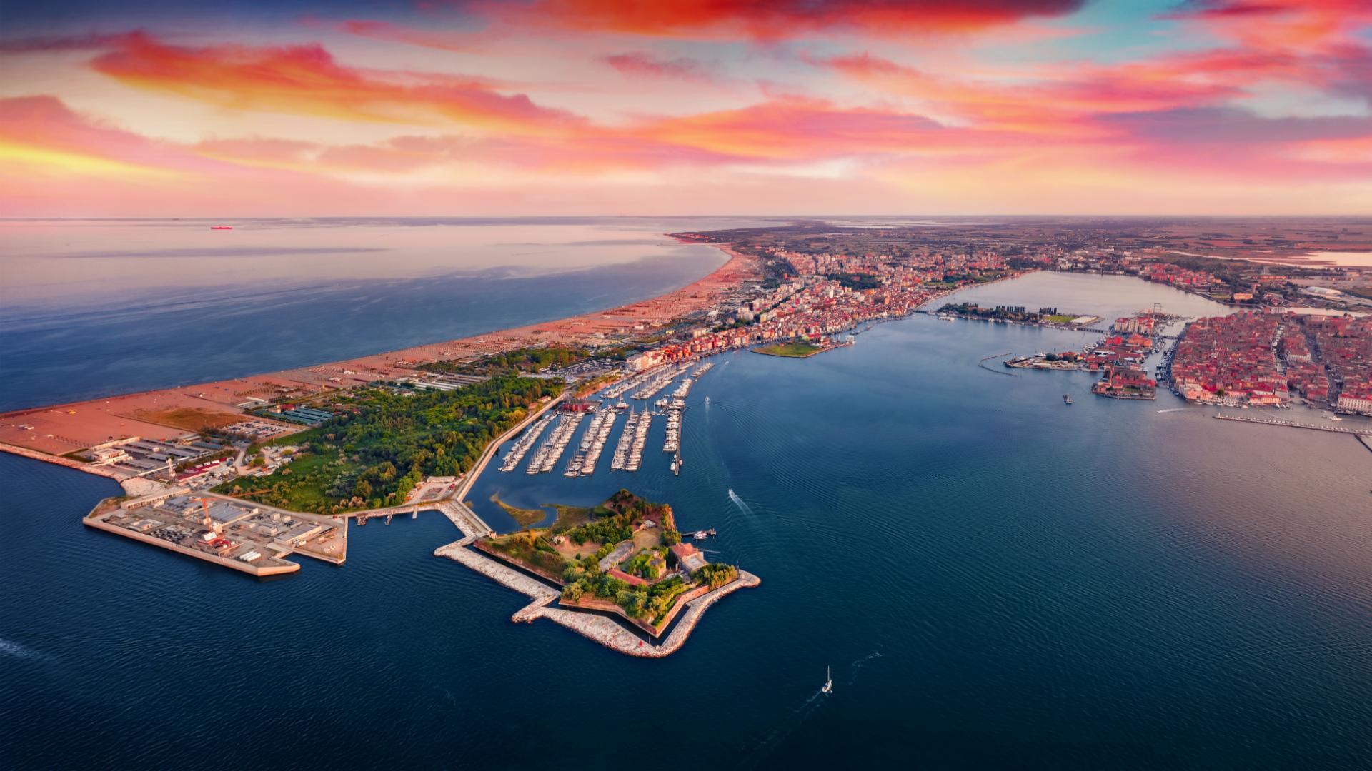 Veduta aerea di una città costiera con porto e tramonto colorato.