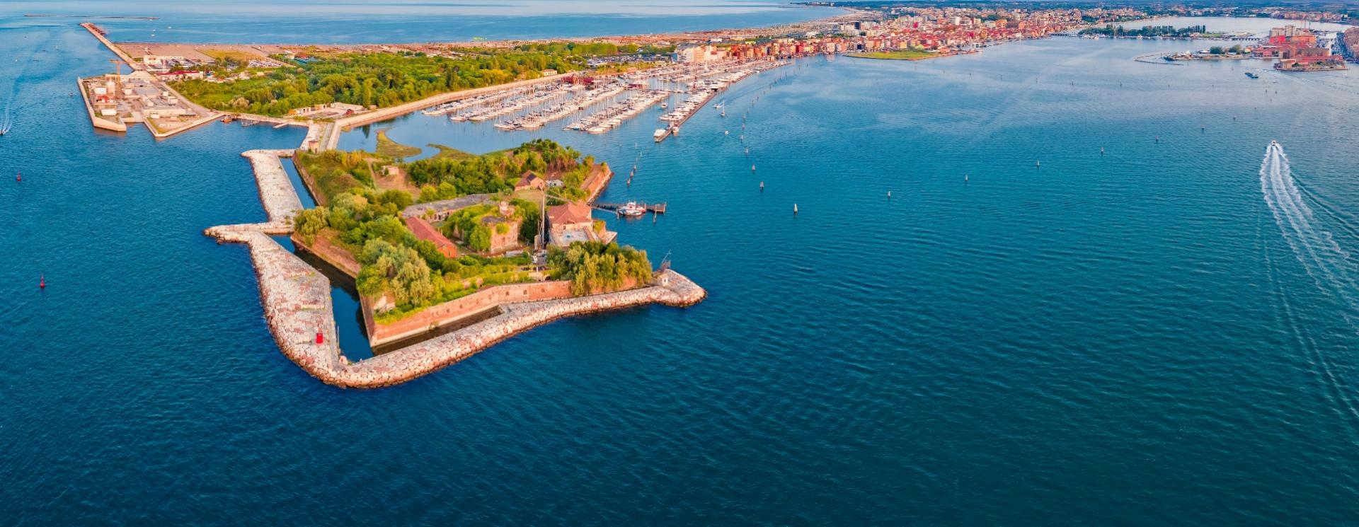 Veduta aerea di un'isola fortificata con porto e città sullo sfondo.