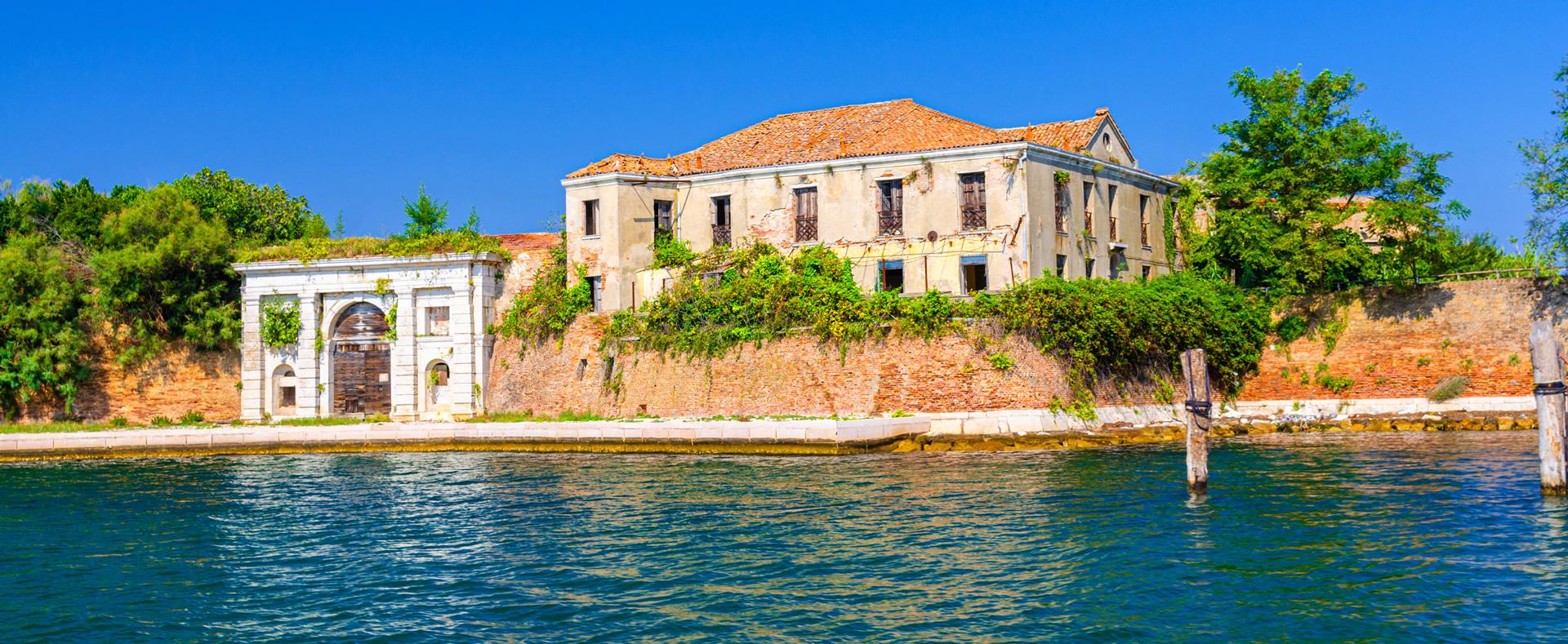 Edificio abbandonato su un'isola, circondato da acqua e vegetazione.