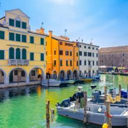 Case colorate lungo un canale con barche ormeggiate, cielo sereno.