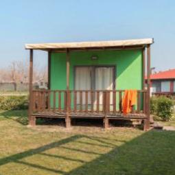 Casetta verde con veranda in legno e prato, sotto un cielo sereno.