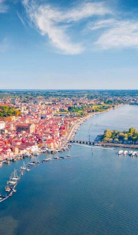 Veduta aerea di una città costiera con spiaggia e porto, cielo sereno.