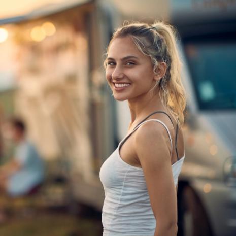 Giovane donna sorridente all'aperto, vicino a un camper, in una giornata soleggiata.