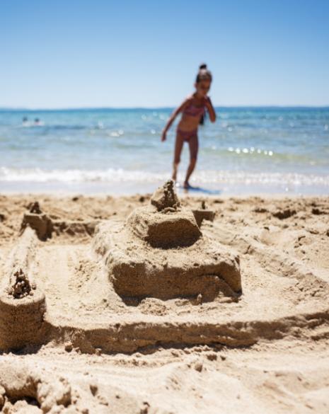 Bambina corre sulla spiaggia vicino a un castello di sabbia.