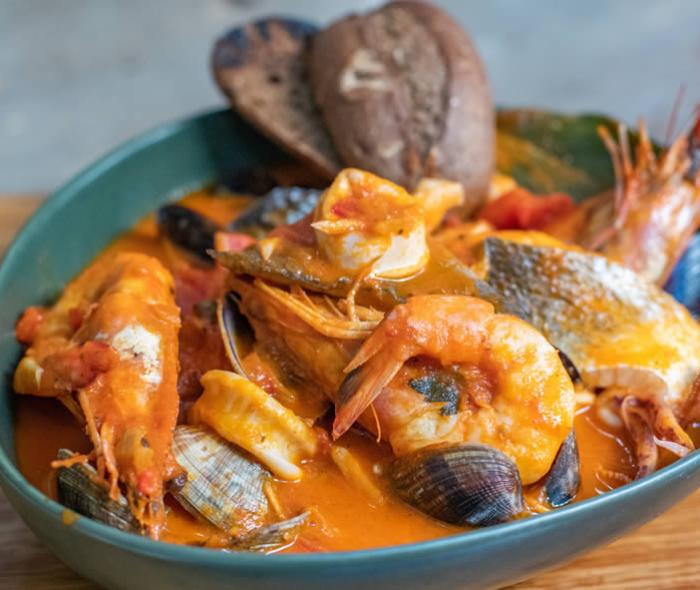 Zuppa di pesce con gamberi, cozze e pane tostato in piatto verde.
