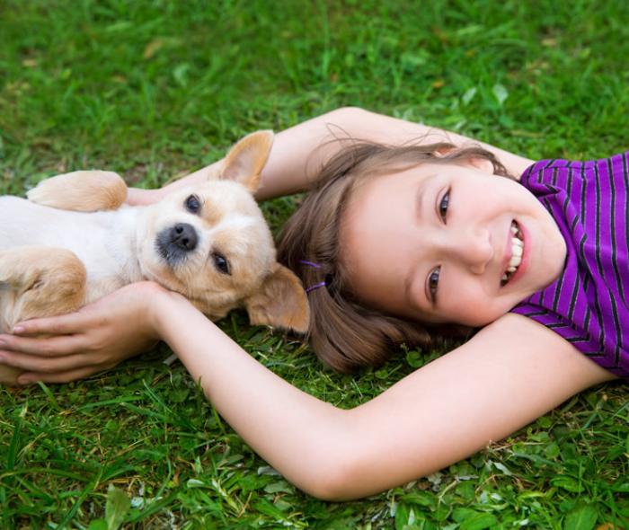 Bambina sorridente abbraccia un cane su un prato verde, trasmettono gioia e serenità.