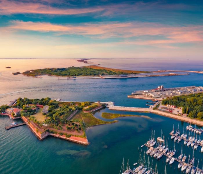 Vista aerea di un'isola con porto turistico e fortificazioni storiche al tramonto.