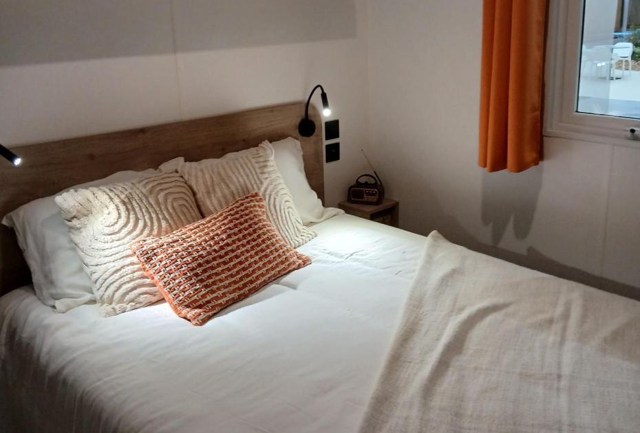 Camera accogliente con letto matrimoniale, cuscini decorativi e tende arancioni.