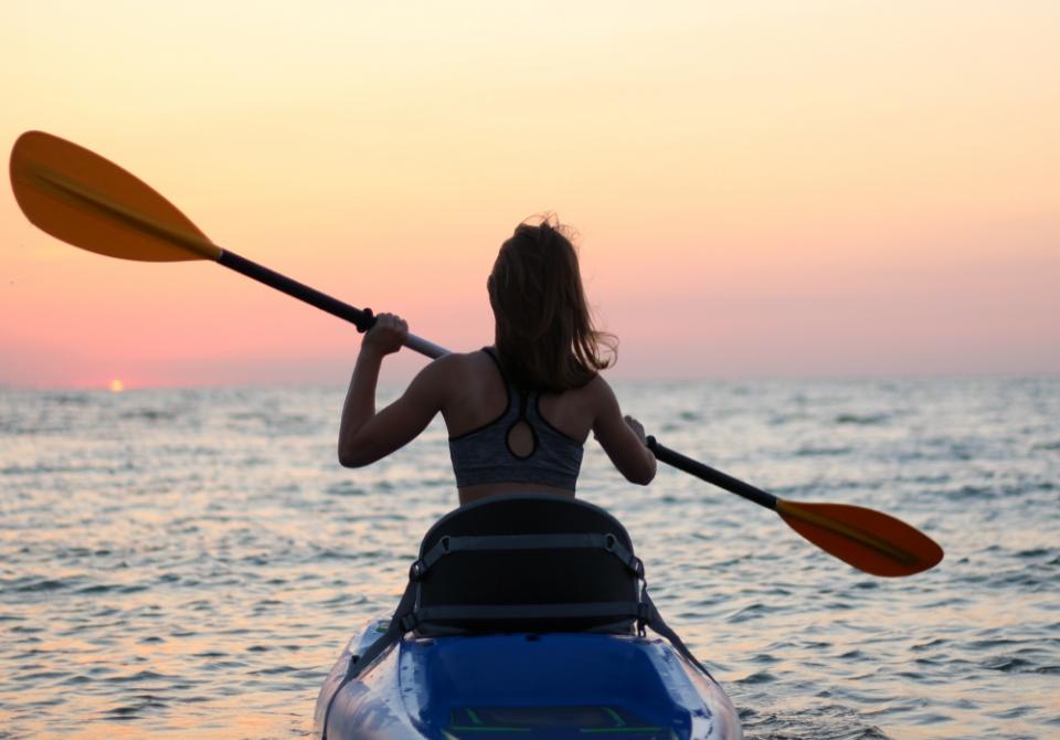 Persona in kayak al tramonto, pagaia sull'acqua calma del mare.